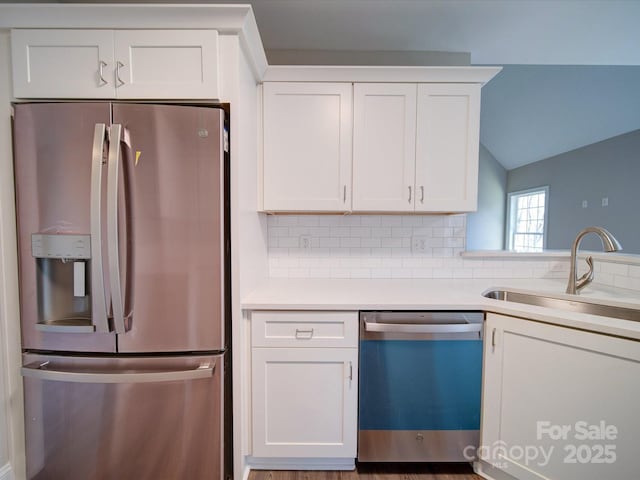 kitchen featuring stainless steel appliances, sink, white cabinets, vaulted ceiling, and decorative backsplash