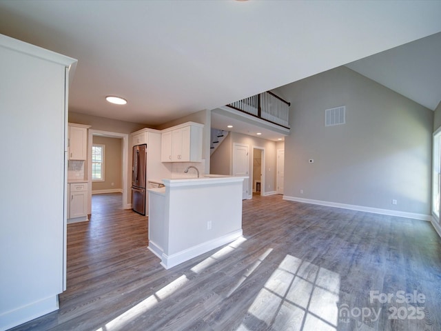 kitchen with sink, white cabinets, light wood-type flooring, tasteful backsplash, and stainless steel refrigerator