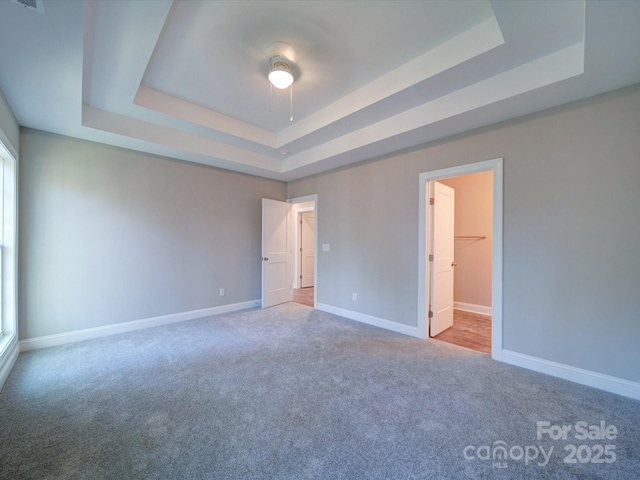 unfurnished bedroom featuring a spacious closet, a raised ceiling, a closet, carpet floors, and ceiling fan