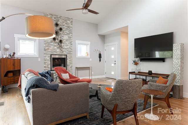 living room with a stone fireplace, ceiling fan, light wood-type flooring, and high vaulted ceiling