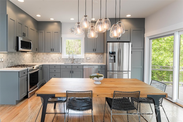 kitchen featuring decorative light fixtures, gray cabinetry, backsplash, sink, and appliances with stainless steel finishes