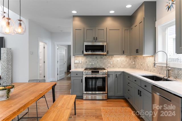 kitchen with appliances with stainless steel finishes, sink, light wood-type flooring, and light stone counters