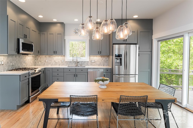 kitchen with a sink, light countertops, stainless steel appliances, gray cabinets, and decorative backsplash