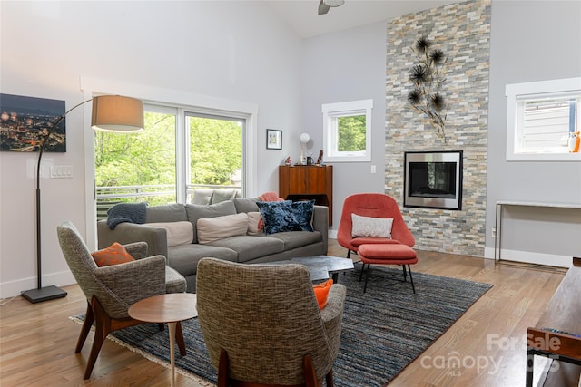 living area with baseboards, a ceiling fan, a fireplace, wood finished floors, and high vaulted ceiling