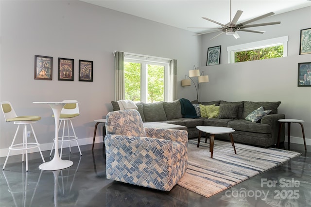 living area featuring finished concrete flooring, baseboards, and ceiling fan