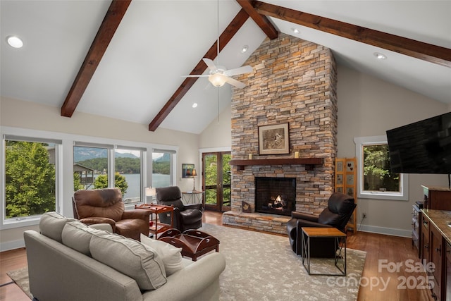 living room featuring a stone fireplace, high vaulted ceiling, beamed ceiling, hardwood / wood-style flooring, and ceiling fan