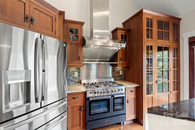 kitchen featuring appliances with stainless steel finishes, tasteful backsplash, ventilation hood, dark stone countertops, and light hardwood / wood-style floors