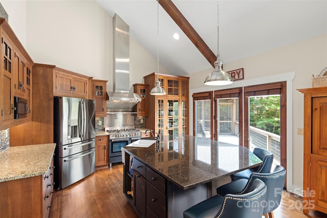 kitchen with beam ceiling, stainless steel appliances, a center island with sink, decorative light fixtures, and wall chimney exhaust hood