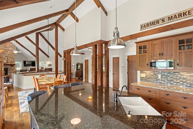 kitchen featuring decorative light fixtures, high vaulted ceiling, stainless steel microwave, a kitchen island with sink, and decorative backsplash