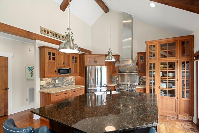 kitchen featuring stainless steel appliances, tasteful backsplash, a center island with sink, dark stone counters, and beamed ceiling