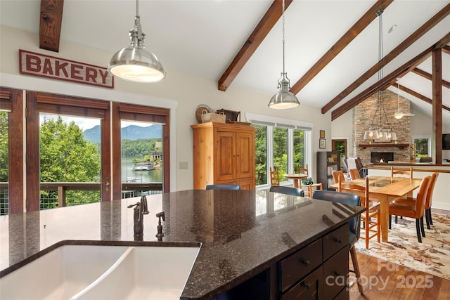 kitchen with sink, a water view, high vaulted ceiling, dark stone countertops, and pendant lighting