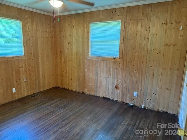 unfurnished room featuring dark wood-type flooring, ornamental molding, ceiling fan, and wood walls