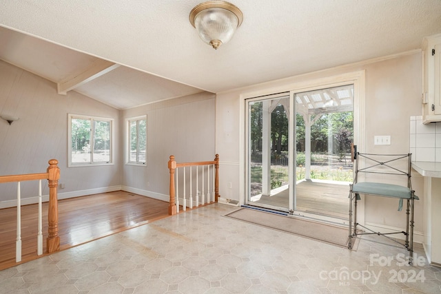 entryway with a textured ceiling, lofted ceiling with beams, and a healthy amount of sunlight