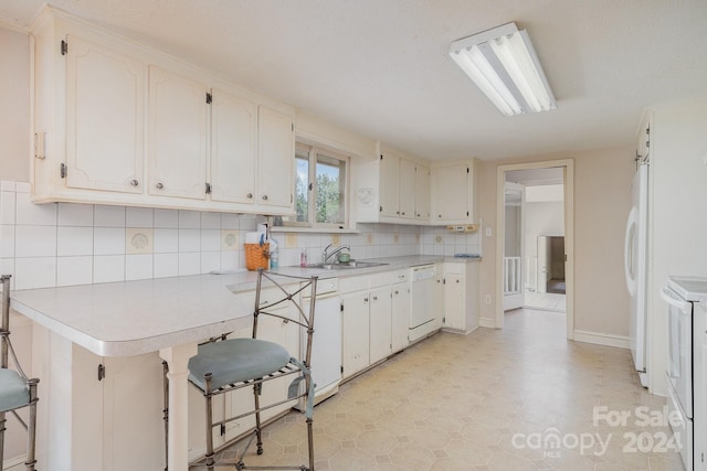 kitchen featuring white appliances, white cabinets, kitchen peninsula, and sink