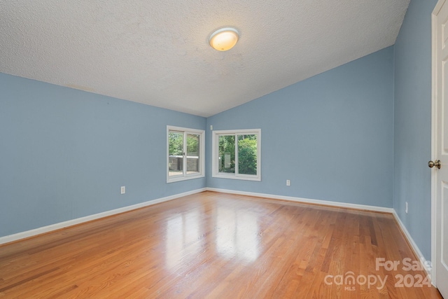 unfurnished room with lofted ceiling, light wood-type flooring, and a textured ceiling