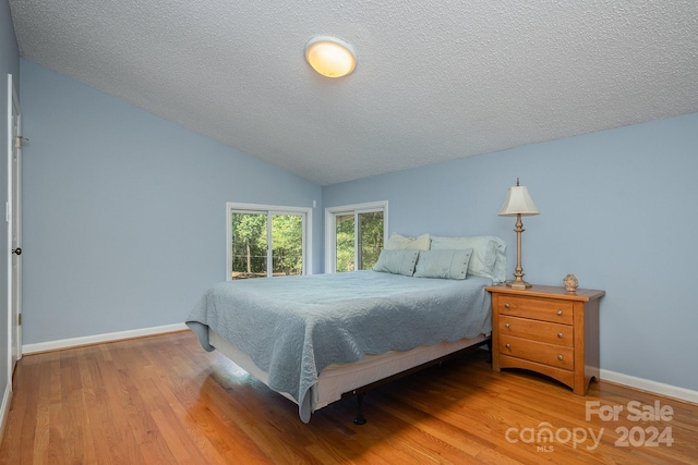 bedroom featuring lofted ceiling, hardwood / wood-style flooring, and a textured ceiling