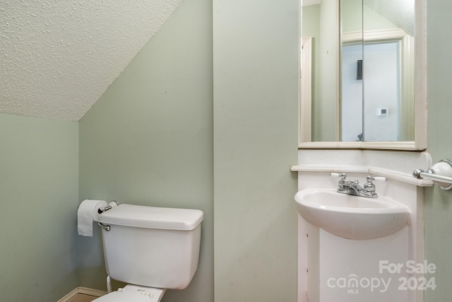 bathroom with toilet, a textured ceiling, sink, and vaulted ceiling