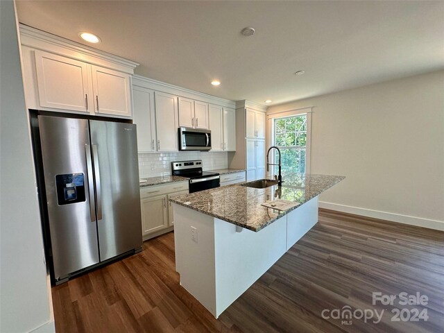 kitchen featuring dark wood-type flooring, sink, white cabinets, stainless steel appliances, and a center island with sink