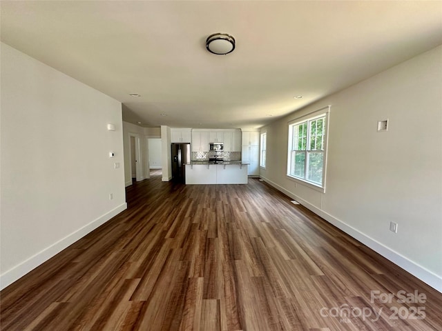 unfurnished living room featuring dark wood-style flooring and baseboards