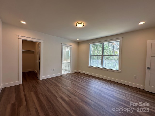 unfurnished bedroom featuring recessed lighting, a walk in closet, baseboards, and dark wood finished floors