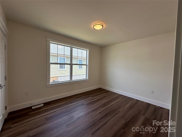 spare room featuring visible vents, baseboards, and dark wood-style floors