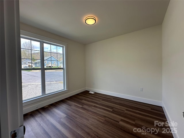 empty room featuring baseboards and dark wood finished floors