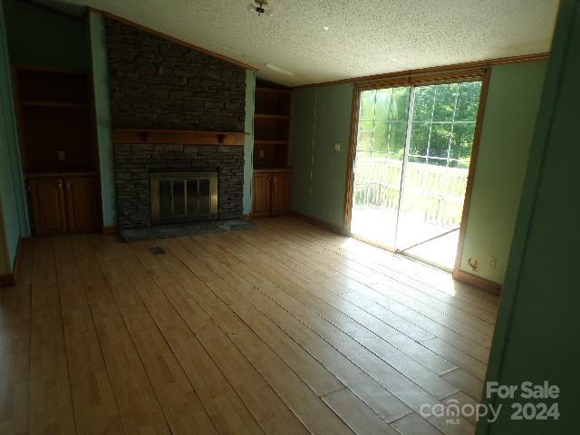 unfurnished living room featuring built in shelves, a stone fireplace, hardwood / wood-style floors, and a textured ceiling