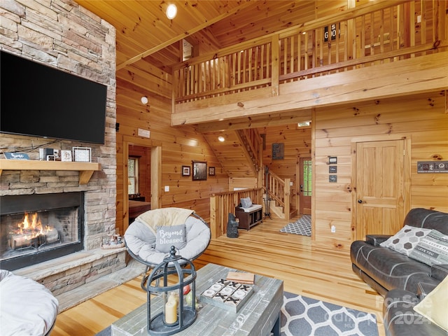 living room with wooden ceiling, hardwood / wood-style flooring, a high ceiling, wood walls, and a stone fireplace