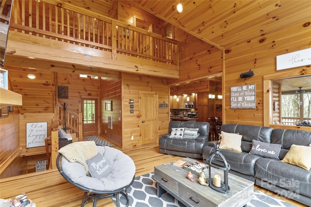 living room featuring a towering ceiling, a wealth of natural light, wooden walls, and light wood-type flooring