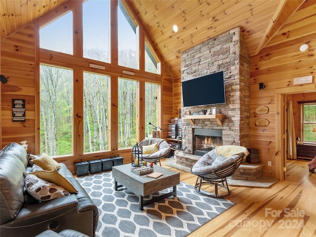 living room featuring a stone fireplace, hardwood / wood-style flooring, wooden walls, and a wealth of natural light