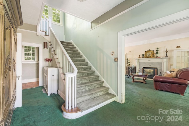 staircase with a brick fireplace, carpet floors, and a healthy amount of sunlight