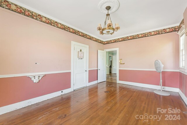 spare room with an inviting chandelier and wood-type flooring