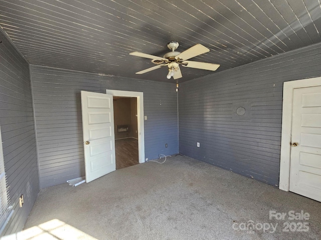 unfurnished bedroom with carpet flooring, wood walls, and ceiling fan