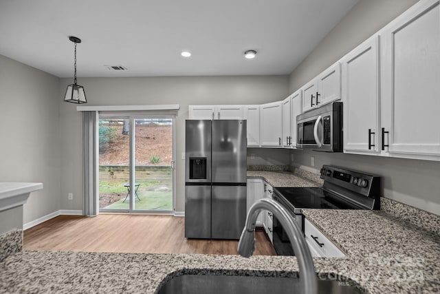 kitchen featuring appliances with stainless steel finishes, light wood-type flooring, white cabinetry, and hanging light fixtures