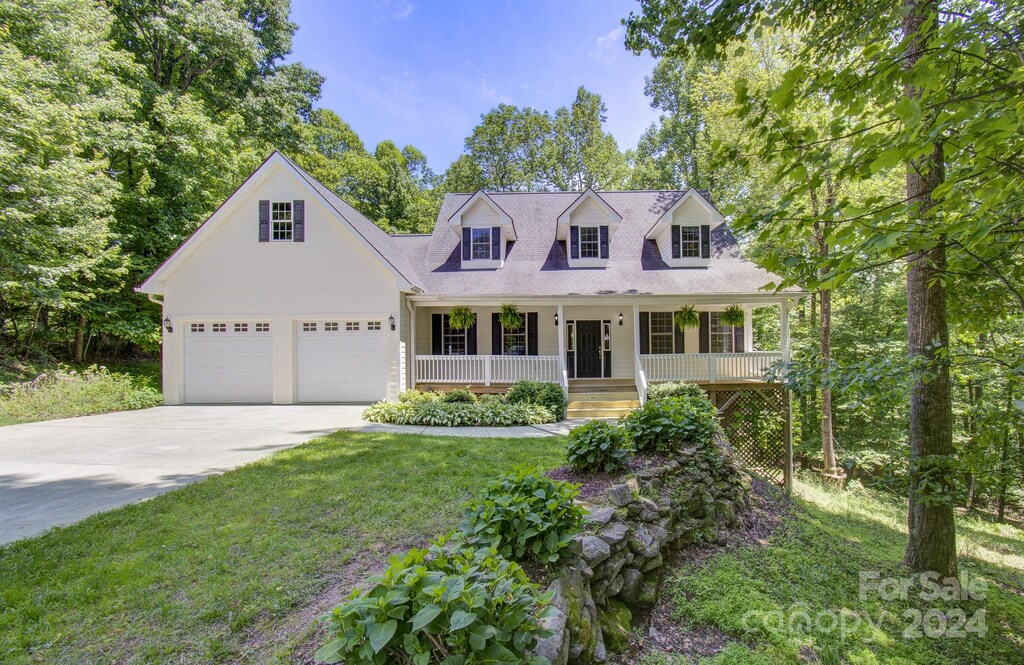 cape cod home with a garage, covered porch, and a front lawn