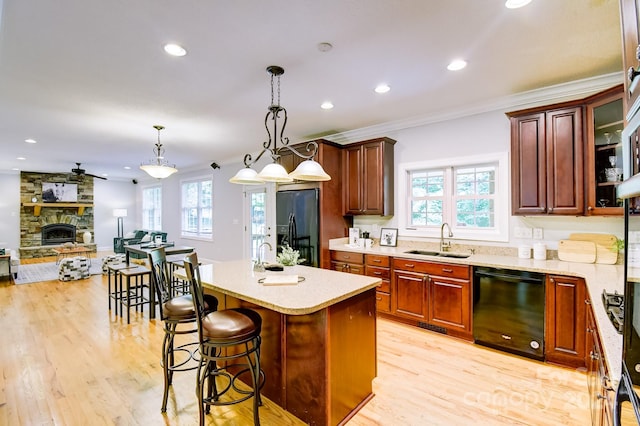 kitchen with light hardwood / wood-style flooring, black appliances, sink, a fireplace, and pendant lighting