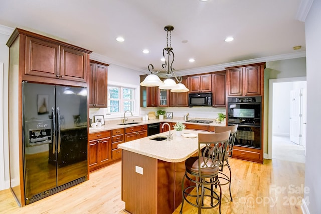 kitchen featuring sink, a kitchen island with sink, light hardwood / wood-style flooring, and black appliances