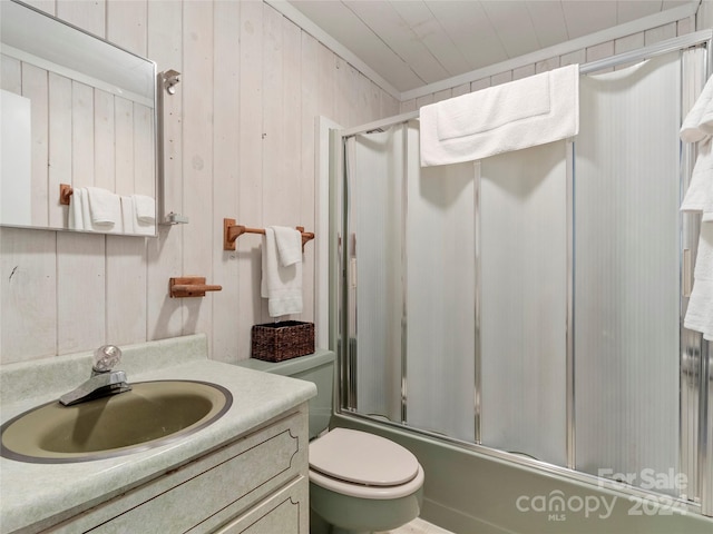 full bathroom featuring vanity with extensive cabinet space, combined bath / shower with glass door, wooden walls, and toilet