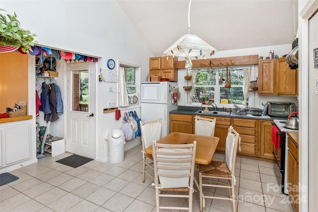 kitchen with light tile patterned floors, hanging light fixtures, white refrigerator, sink, and high vaulted ceiling