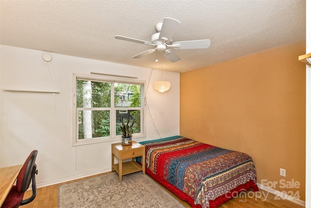 bedroom with a ceiling fan, a textured ceiling, baseboards, and wood finished floors