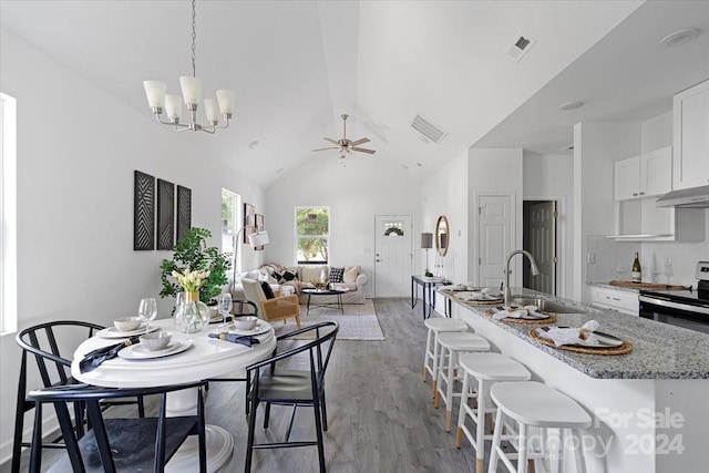 dining space featuring ceiling fan with notable chandelier, light hardwood / wood-style floors, high vaulted ceiling, and sink