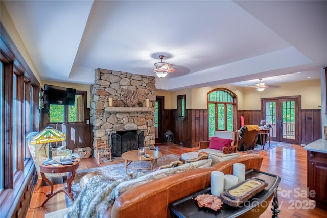 living room with a raised ceiling, ceiling fan, french doors, and a stone fireplace