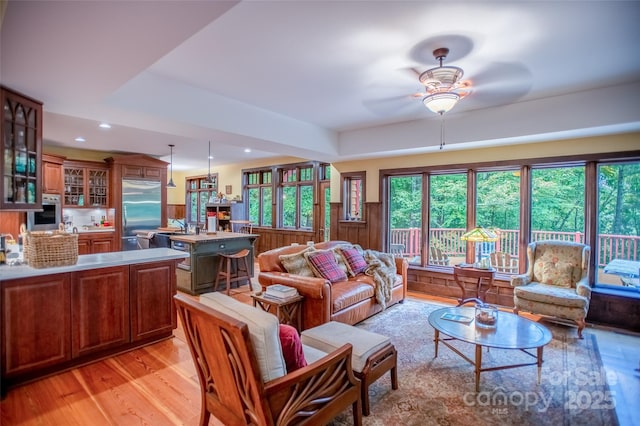 living room featuring light wood-type flooring, ceiling fan, and wooden walls