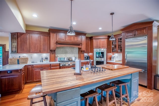 kitchen with pendant lighting, appliances with stainless steel finishes, wooden counters, a kitchen island, and light hardwood / wood-style floors