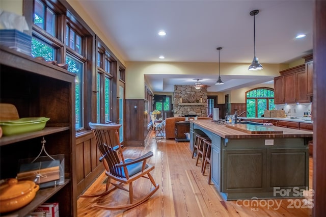 kitchen featuring ceiling fan, wood walls, a center island with sink, butcher block countertops, and light wood-type flooring