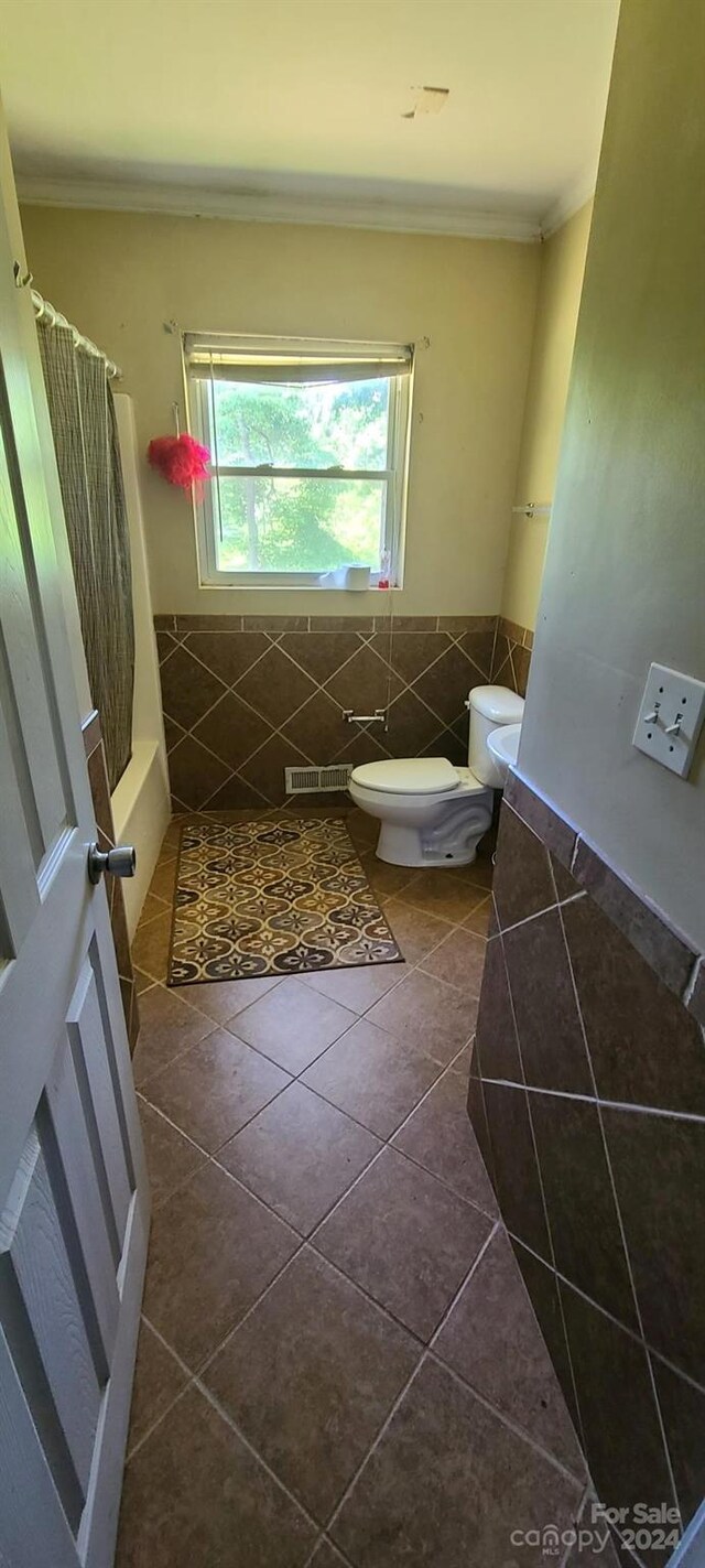 bathroom featuring toilet, ornamental molding, tile patterned floors, and tile walls