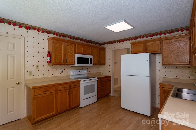 kitchen featuring a textured ceiling, sink, white appliances, and light wood-type flooring