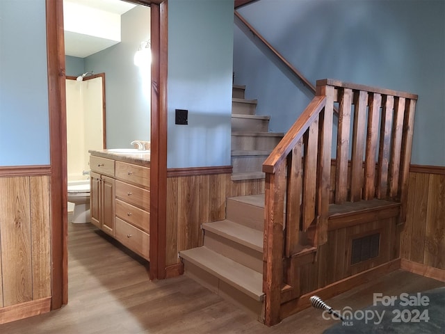 staircase featuring sink, wood-type flooring, and wood walls