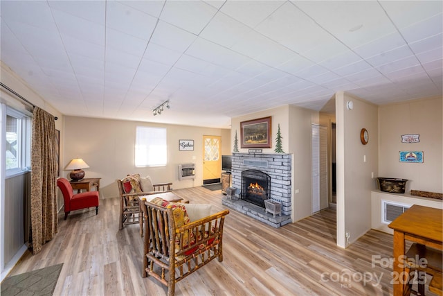 living room with a stone fireplace, light hardwood / wood-style flooring, rail lighting, and heating unit