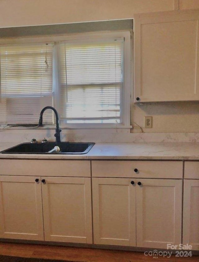 kitchen featuring light stone counters, white cabinetry, and sink